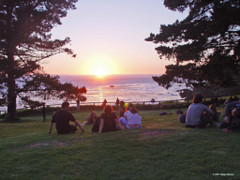 Esalen people on lawn watching sun set over ocean.